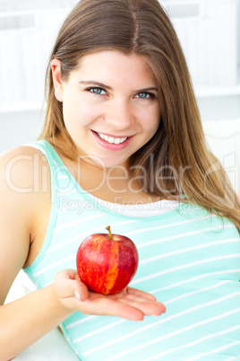 Pretty caucasian woman holding an apple sitting on a sofa
