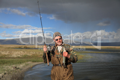 Fisherman with spinning catching fish in mountain lake Dayan Nuu