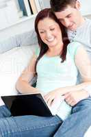 Positive couple using laptop smiling at the camera sitting on a