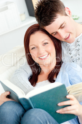 Charming young couple reading a book lying on the sofa