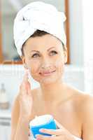 Positive young woman with a towel putting cream on her face in t
