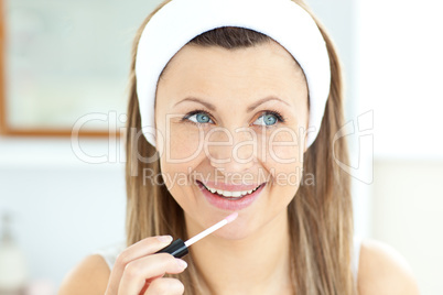Charming woman applying gloss on her lips in the bathroom