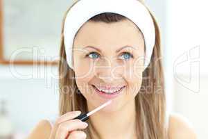 Charming woman applying gloss on her lips in the bathroom