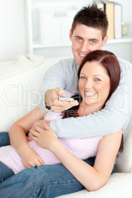 Portrait of an smiling couple watching television lying on the s