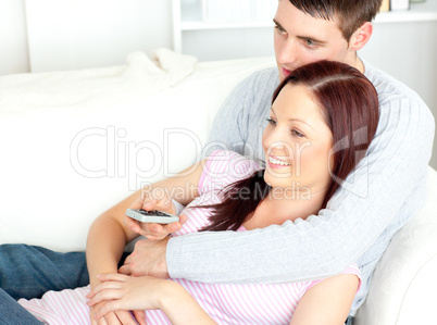 Portrait of an embracing couple watching television lying on the