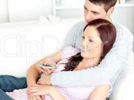 Portrait of an embracing couple watching television lying on the