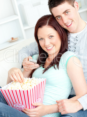 Kind couple eating popcorn and watching television lying on the