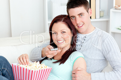 Hugging couple eating popcorn and watching television lying on t