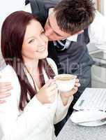 Handsome businessman kissing his girlfriend who is holding a cup