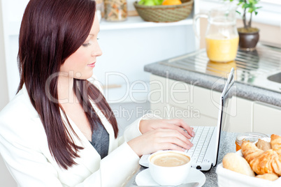 Positive businesswoman using her laptop during breakfast