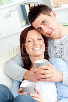 Positive young couple drinking coffee on a sofa smiling at the c