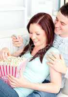 Bright young couple lying on the sofa with popcorn and remote