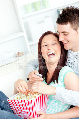 Laughing young couple lying on the sofa with popcorn and remote
