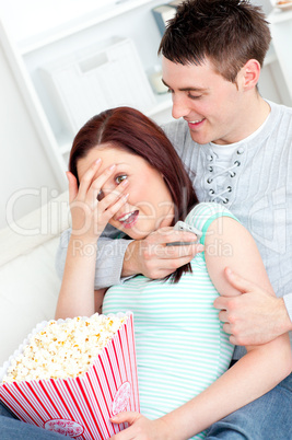 Young couple lying on the sofa with popcorn and remote