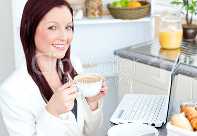 Glowing businesswoman drinking coffee smiling at the camera sitt