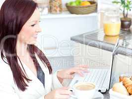 Glowing businesswoman using her laptop and holding a cup of coff