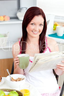 Bright woman eating cereals while reading newspaper in the kitch