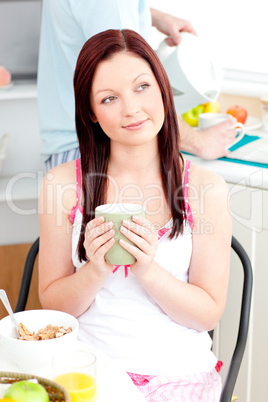 Pensive woman eating her breakfast at home holding a cup of coff