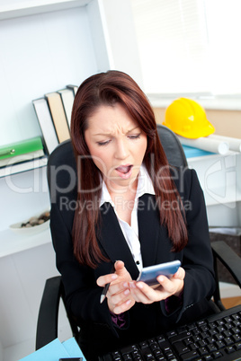 Astonished businesswoman looking at her calculator sititng at he