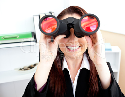 Young businesswoman using binoculars in her office stting at her