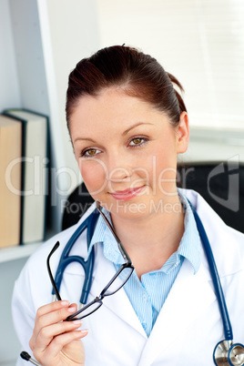 Happy female doctor holding glasses smiling at the camera sittin