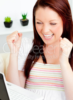 Ecstatic young woman using her laptop sitting on a sofa at home