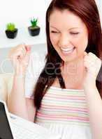 Ecstatic young woman using her laptop sitting on a sofa at home