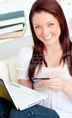 Happy woman with a credit card and a laptop on a sofa at home