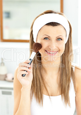 Smiling caucasian woman putting powder on her face smiling at th