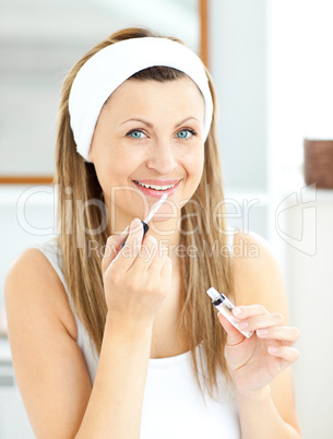 Bright woman applying gloss on her lips in the bathroom