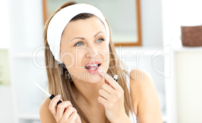 Pretty woman applying gloss on her lips in the bathroom