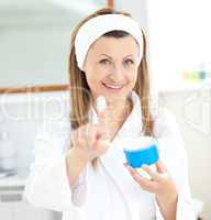 Pretty young woman using cream wearing a bath robe in the bathro