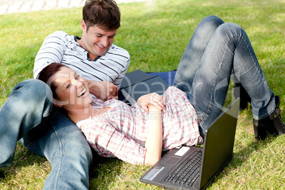 Couple of bright students using a laptop lying on the grass