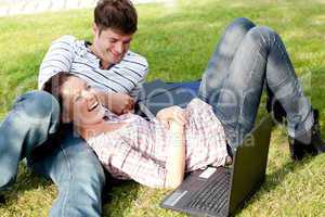 Couple of bright students using a laptop lying on the grass