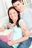 Hugging couple eating popcorn and watching television lying on t