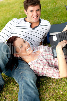 Couple of happy students using a laptop lying on the grass