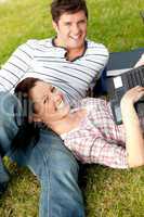 Couple of happy students using a laptop lying on the grass