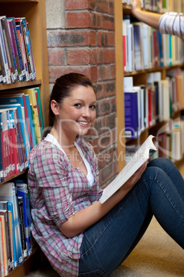 Smiling young woman reading a book sitting on the floor