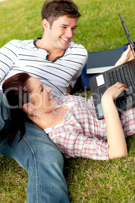 Couple of positive students using a laptop lying on the grass