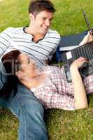 Couple of positive students using a laptop lying on the grass
