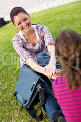 Two female students talking together sitting on the grass