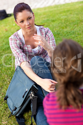 Two female friends talking together sitting on the grass