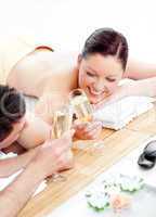 Loving young couple drinking champagne lying on a massage table