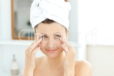 Pretty young woman with a towel putting cream on her face in the
