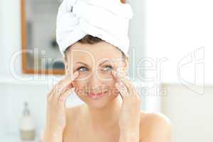 Pretty young woman with a towel putting cream on her face in the