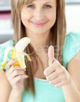 Smiling woman with thumb up holding a banana in the kitchen