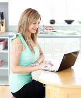 Delighted blond woman using her laptop smiling at the camera at