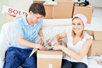 Joyful caucasian couple unpacking boxes with glasses