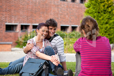 Happy couple of students sitting on grass talking with a female