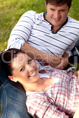 Joyful couple of students sitting on grass and smiling at the ca